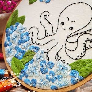 May include: Embroidered hoop art featuring a white octopus with black outlines and blue and white flowers with green leaves.