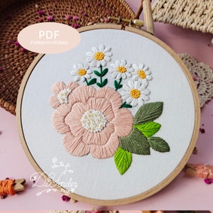 May include: Embroidered hoop art featuring a pink flower with white centers and green leaves. The hoop is made of wood and has a white fabric background. The text "PDF Pattern+Video" is visible in the upper left corner of the image.