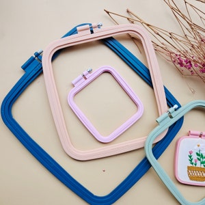 May include: Three embroidery hoops in different sizes. The largest hoop is blue, the middle hoop is pink, and the smallest hoop is light green. The hoops are nested inside each other.