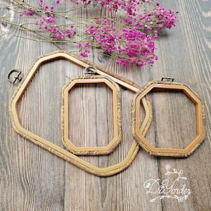 Op de afbeelding: Drie houten borduurringen in verschillende maten, met een bruin houtnerfpatroon en messing beslag. De ringen liggen op een houten oppervlak.