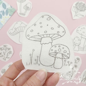 Peut inclure: Un tissu blanc avec deux broderies de champignons noirs et blancs. Le plus grand champignon a un chapeau rouge à pois et le plus petit champignon a un chapeau blanc à pois.