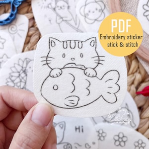 May include: A collection of white embroidery stickers with black line drawings of various designs, including a cat holding a fish. The stickers are labeled "PDF Embroidery sticker stick & stitch".