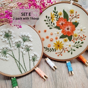 Peut inclure: Deux cerceaux &agrave; broder avec des motifs floraux. Le cerceau de gauche pr&eacute;sente des fleurs blanches avec des tiges vertes. Le cerceau de droite pr&eacute;sente des fleurs orange, jaunes et blanches avec des tiges vertes. Le texte "SET E 2 pack with 1 hoop" est visible sur l'image.