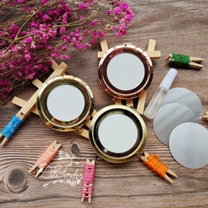 May include: Three round, gold-toned compact mirrors with different coloured rims. The mirrors are on a wooden stand with colourful yarn and clips.