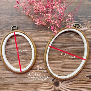 Może przedstawiać: Dwa tamborki do haftu z drewnianymi ramami i białymi wewnętrznymi obręczami. Większy tamborek ma średnicę 13,5 cm, a mniejszy 13,3 cm.