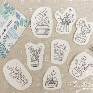 Peut inclure: Huit dessins au trait noir et blanc de plantes en pot sur du papier blanc. Les dessins comprennent un cactus, un champignon et diverses plantes feuillues. Le papier est sur une surface à motifs floraux.
