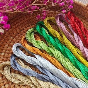 May include: A collection of ten spools of metallic embroidery floss in various colors, including gold, silver, red, green, and purple. The spools are arranged in a rainbow pattern on a woven basket.