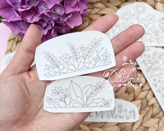 Op de afbeelding: Twee witte stoffen met zwarte lijntekeningen van bloemmotieven. De ontwerpen zijn verschillende arrangementen van bloemen, bladeren en stengels.