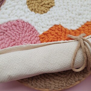 May include: A close-up of a beige canvas with a colorful geometric design created with yarn. The canvas is rolled up and tied with a brown string.