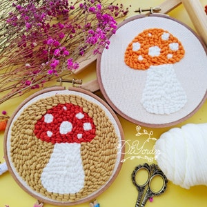 May include: Two mushroom-themed embroidery hoops. One features a red mushroom with white spots and a tan background. The other has an orange mushroom with white spots and a white background. Both are in wooden hoops.