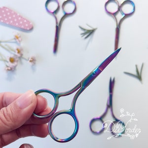 Pode incluir: Cinco pequenas tesouras arco-íris com pontas afiadas. As tesouras são de metal e têm um acabamento brilhante.