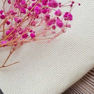 May include: A close-up of a white fabric with a fine weave texture. A bouquet of pink dried flowers is placed on top of the fabric.
