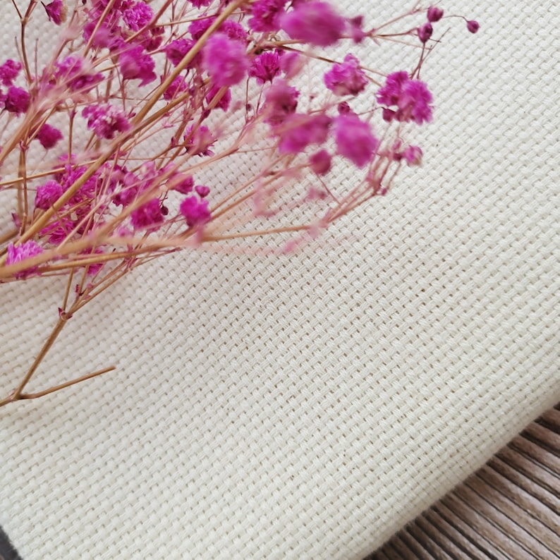 May include: A close-up of a white fabric with a fine weave texture. A bouquet of pink dried flowers is placed on top of the fabric.