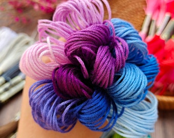 Peut inclure: Un assortiment de bobines de fil à broder dans différentes nuances de violet, bleu et rose. Le fil est enroulé en forme de fleur.