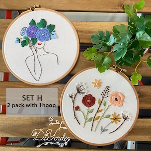 Peut inclure: Deux cerceaux &agrave; broder avec des motifs floraux. Le premier cerceau pr&eacute;sente un dessin au trait d'une femme avec des fleurs bleues qui lui couvrent le visage. Le deuxi&egrave;me cerceau pr&eacute;sente une vari&eacute;t&eacute; de fleurs color&eacute;es avec des tiges et des feuilles vertes. Le texte "SET H 2 pack with 1 hoop" est situ&eacute; sous les cerceaux.