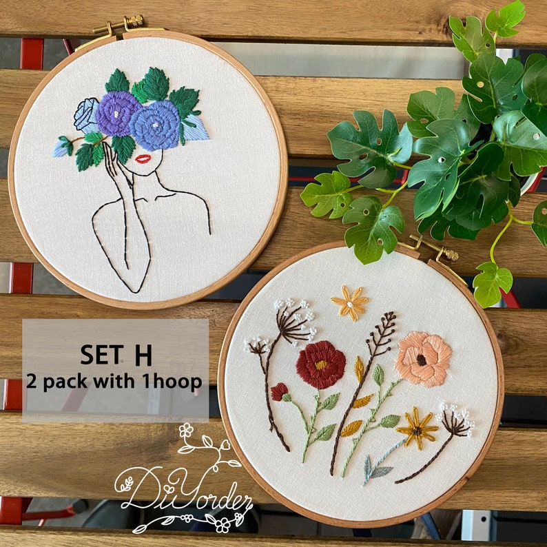 Peut inclure: Deux cerceaux &agrave; broder avec des motifs floraux. Le premier cerceau pr&eacute;sente un dessin au trait d'une femme avec des fleurs bleues qui lui couvrent le visage. Le deuxi&egrave;me cerceau pr&eacute;sente une vari&eacute;t&eacute; de fleurs color&eacute;es avec des tiges et des feuilles vertes. Le texte "SET H 2 pack with 1 hoop" est situ&eacute; sous les cerceaux.