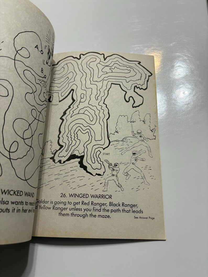 May include: A black and white maze with a winged warrior design. The maze has a start point and a finish point. The text "26. WINGED WARRIOR" is at the top of the maze. The text "Goldar is going to get Red Ranger, Black Ranger, and Yellow Ranger unless you find the path that leads them through the maze." is below the maze.