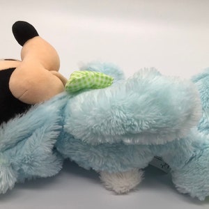 K&ouml;nnte beinhalten: Ein blauer Pl&uuml;schhase mit einer gr&uuml;n-wei&szlig; karierten Schleife. Der Hase hat einen Mickey Mouse Kopf mit schwarzen Ohren und einer schwarzen Nase.