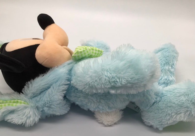 K&ouml;nnte beinhalten: Ein blauer Pl&uuml;schhase mit einer gr&uuml;n-wei&szlig; karierten Schleife. Der Hase hat einen Mickey Mouse Kopf mit schwarzen Ohren und einer schwarzen Nase.