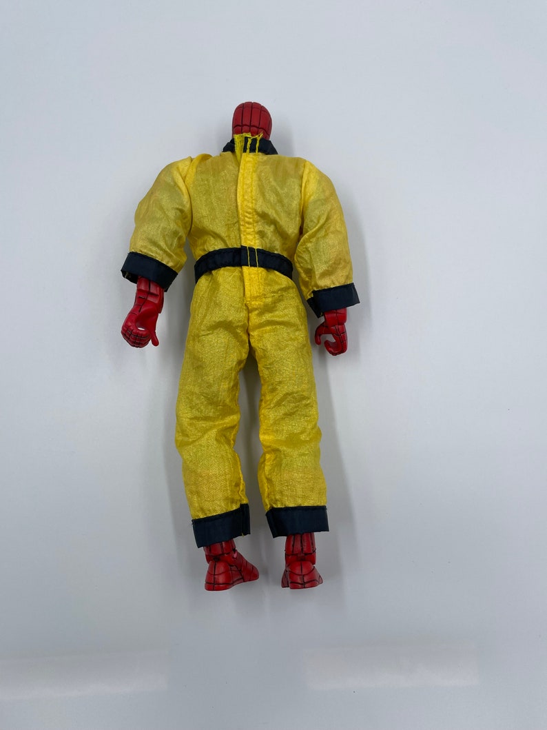 Puede incluir: Una figura de acci&oacute;n roja y azul que lleva un mono amarillo con ribetes negros. La figura est&aacute; de pie sobre un fondo blanco.