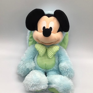 K&ouml;nnte beinhalten: Ein blauer Pl&uuml;sch-Osterhase mit einer gr&uuml;n-wei&szlig; karierten Schleife. Der Hase hat Mickey Mouse Ohren und ein schwarzes Gesicht.