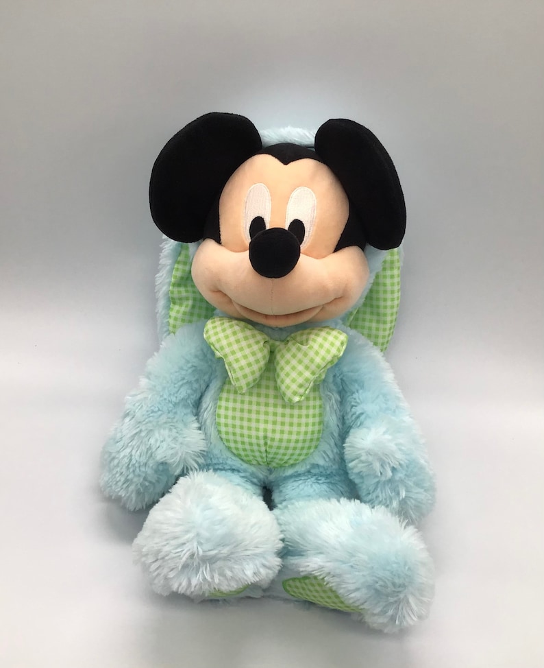 K&ouml;nnte beinhalten: Ein blauer Pl&uuml;sch-Osterhase mit einer gr&uuml;n-wei&szlig; karierten Schleife. Der Hase hat Mickey Mouse Ohren und ein schwarzes Gesicht.