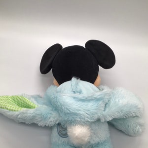 K&ouml;nnte beinhalten: Ein blaues Pl&uuml;sch-Hasenkost&uuml;m mit einem wei&szlig;en Bommel-Schwanz. Das Kost&uuml;m wird von einer schwarzen Pl&uuml;sch-Mickey Mouse mit gro&szlig;en Ohren getragen.