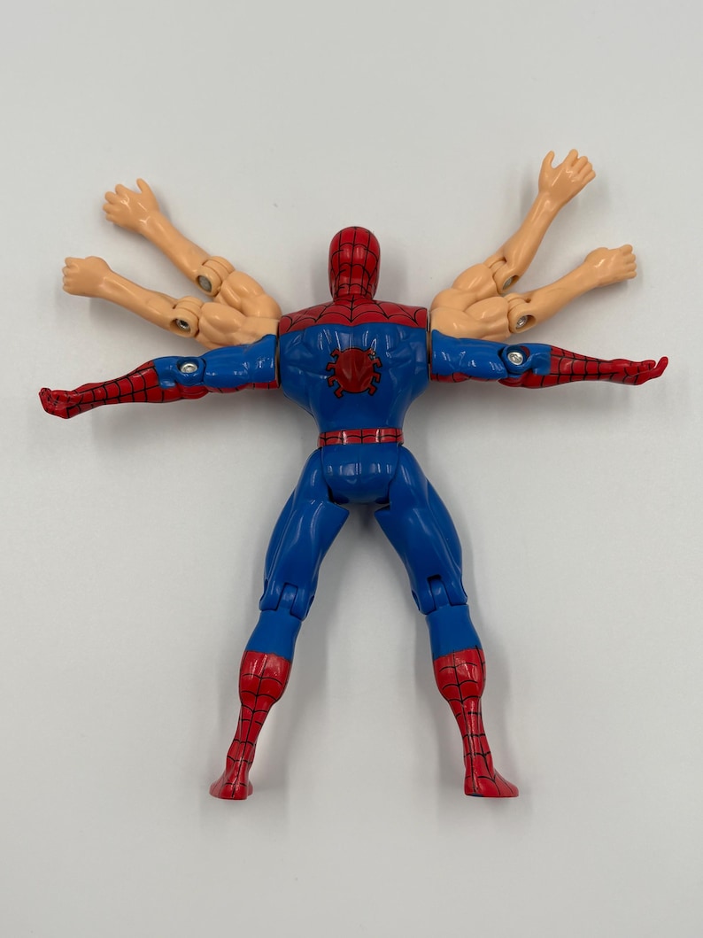 May include: A blue, red, and tan Spider-Man action figure with multiple arms. The figure has a red mask and spider emblem on the chest. The legs and arms are articulated.