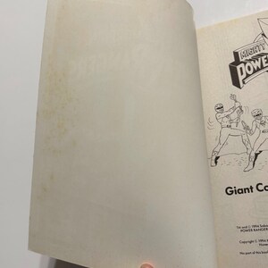 May include: An open book with a black and white illustration of two Power Rangers fighting. The book cover features the Mighty Morphin Power Rangers logo and the text "Giant Combat". The copyright information is printed on the bottom of the page: "TM and &copy; 1994 Saban Entertainment, Inc. POWER RANGER. Copyright &copy; 1994 Home Box Office, Inc. No part of this book may be reproduced..."