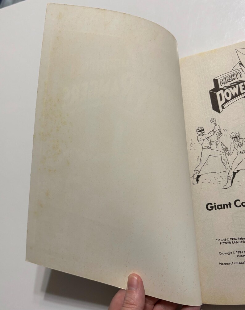May include: An open book with a black and white illustration of two Power Rangers fighting. The book cover features the Mighty Morphin Power Rangers logo and the text "Giant Combat". The copyright information is printed on the bottom of the page: "TM and &copy; 1994 Saban Entertainment, Inc. POWER RANGER. Copyright &copy; 1994 Home Box Office, Inc. No part of this book may be reproduced..."