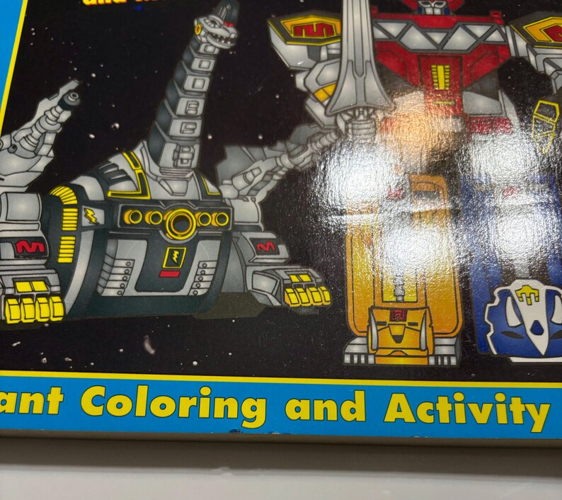 May include: A coloring and activity book featuring the Power Rangers. The cover shows a black and yellow robot with a red and silver robot in the background. The book has a blue border with the text "Giant Coloring and Activity" on the bottom.