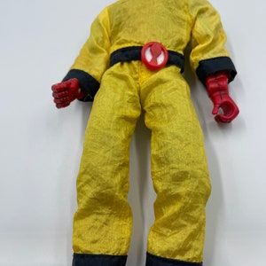 Puede incluir: Un mono amarillo con ribetes negros y un s&iacute;mbolo de ara&ntilde;a roja en el cintur&oacute;n. La figura lleva una m&aacute;scara y guantes rojos.