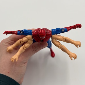 May include: A red, blue, and tan Spider-Man action figure with multiple arms. The figure has a red spider-web design on the chest and head. The arms are in various positions, with some extended and others bent.