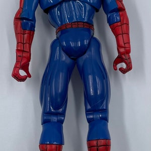 Puede incluir: Una figura de acci&oacute;n de pl&aacute;stico roja y azul de Spider-Man. La figura est&aacute; en posici&oacute;n con los brazos a los lados y las piernas separadas. La figura tiene un dise&ntilde;o de telara&ntilde;a en el pecho y un logotipo de ara&ntilde;a en la espalda.