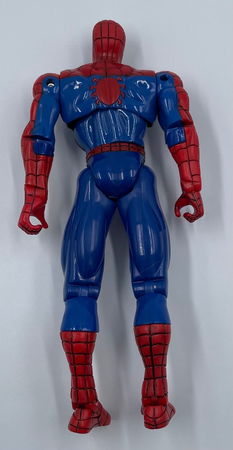 Puede incluir: Una figura de acci&oacute;n de pl&aacute;stico roja y azul de Spider-Man. La figura est&aacute; en posici&oacute;n con los brazos a los lados y las piernas separadas. La figura tiene un dise&ntilde;o de telara&ntilde;a en el pecho y un logotipo de ara&ntilde;a en la espalda.