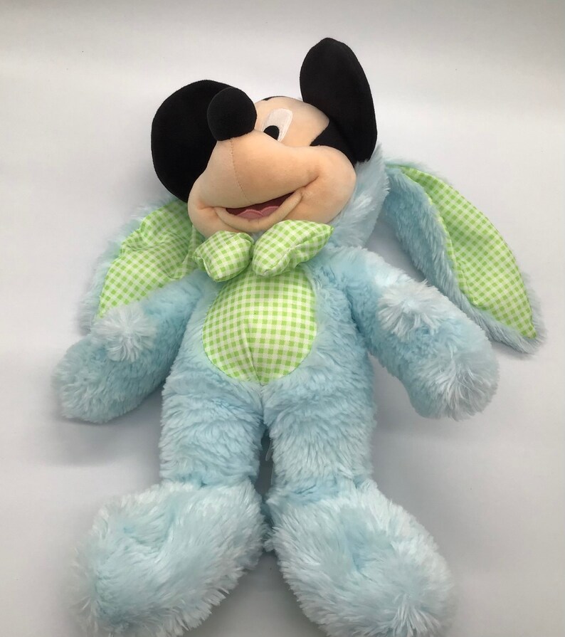 K&ouml;nnte beinhalten: Ein blauer Pl&uuml;sch-Mickey Mouse, der ein gr&uuml;nes und wei&szlig;es Gingham-Kaninchenkost&uuml;m tr&auml;gt. Die Hasenohren sind lang und schlaff.