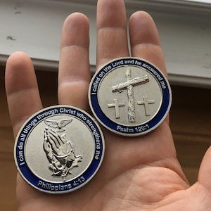 May include: Two silver-colored metal tokens with blue trim. The first token features a praying hand with a dove and rosary beads. The text on the token reads "I can do all things through Christ who strengthens me" and "Philippians 4:13". The second token features a cross with the text "I called on the Lord and he answered me" and "Psalm 120:1".
