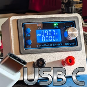 May include: A white and grey Buck-Boost ZK-4KX power supply with a digital display showing voltage and amperage. It has blue buttons and a silver knob. A USB-C connector is in the foreground, with the text "USB C" below.