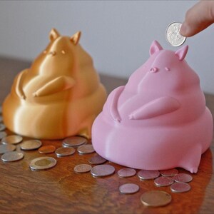 Gold and light pink piggy bank surrounded by coins with a hand dropping a coin into the piggy bank