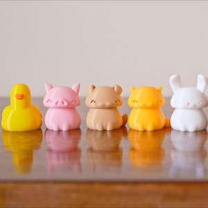 Peut inclure: Un ensemble de sept petites figurines d'animaux imprim&eacute;es en 3D et color&eacute;es. Les figurines comprennent un canard, un cochon, un ours, un lapin, un chat et deux autres animaux. Les figurines sont toutes souriantes et ont un style cartoon.