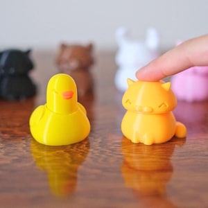 Peut inclure: Une collection de petites figurines d'animaux en 3D imprim&eacute;es en couleur, comprenant un canard, un chat, un lapin, un ours et un cygne. Les figurines sont dispos&eacute;es sur une surface en bois.