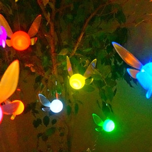 May include: A string of fairy lights shaped like the iconic video game character, the fairy, with glowing multi-colored bulbs. The lights are hanging from a tree branch.