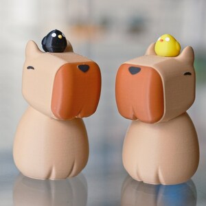 May include: Two brown ceramic figurines of dogs with small bird figurines on their heads. One dog has a black bird and the other has a yellow bird.