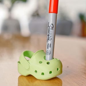 May include: A green plastic shoe with a red and gray Sharpie marker inserted into the top opening.