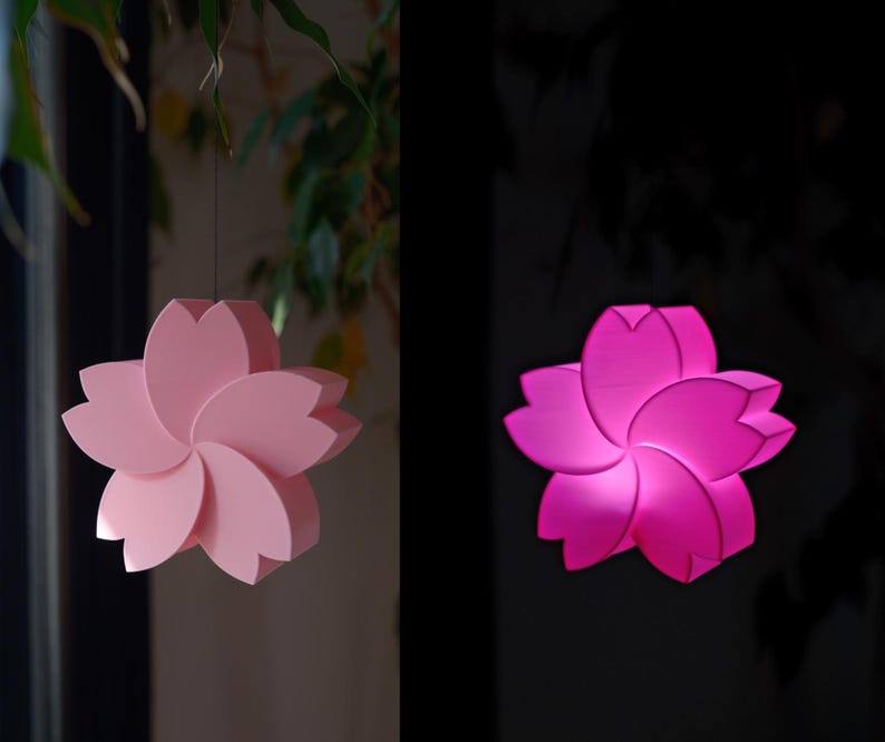 May include: A pink paper flower lampshade with a 3D design. The lampshade is hanging from the ceiling and is lit up, casting a warm glow.