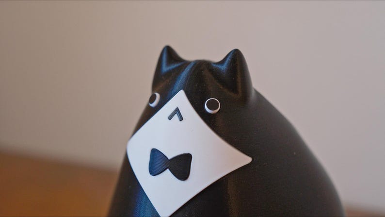 May include: A black and white cat figurine with a tuxedo design. The cat has a white bib with a black bow tie, and round eyes. The ears are pointed, and the figurine has a smooth finish. The cat is a decorative item.