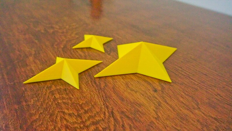 May include: Three yellow paper stars of different sizes on a wooden surface.