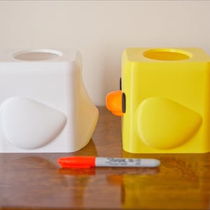 Pu&ograve; includere: Due copri scatola di fazzoletti a forma di pulcini dei cartoni animati. Uno &egrave; bianco e l'altro &egrave; giallo.