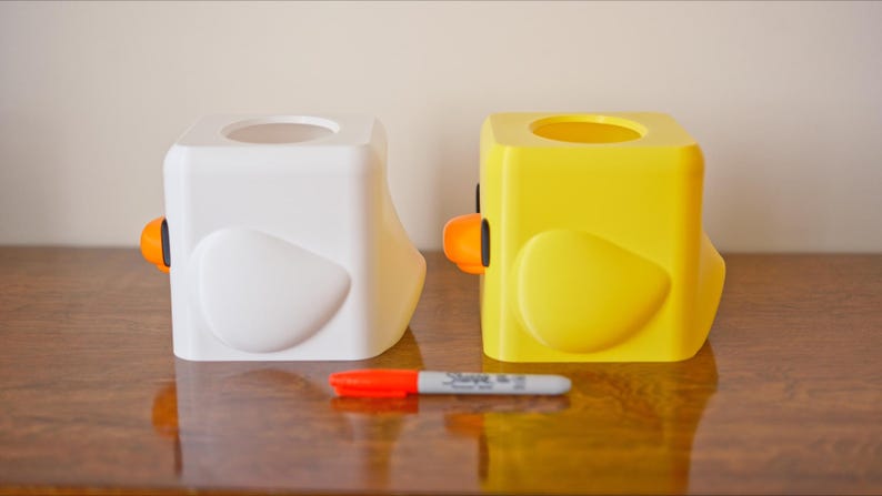Pu&ograve; includere: Due copri scatola di fazzoletti a forma di pulcini dei cartoni animati. Uno &egrave; bianco e l'altro &egrave; giallo.