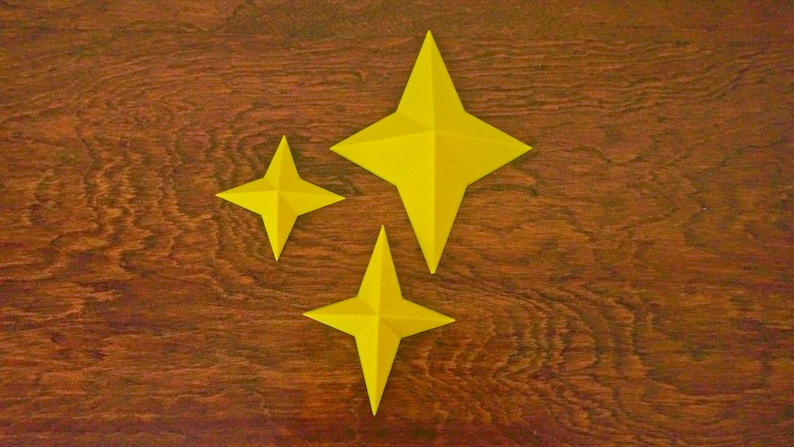 May include: Three yellow paper stars of different sizes on a brown wooden background.
